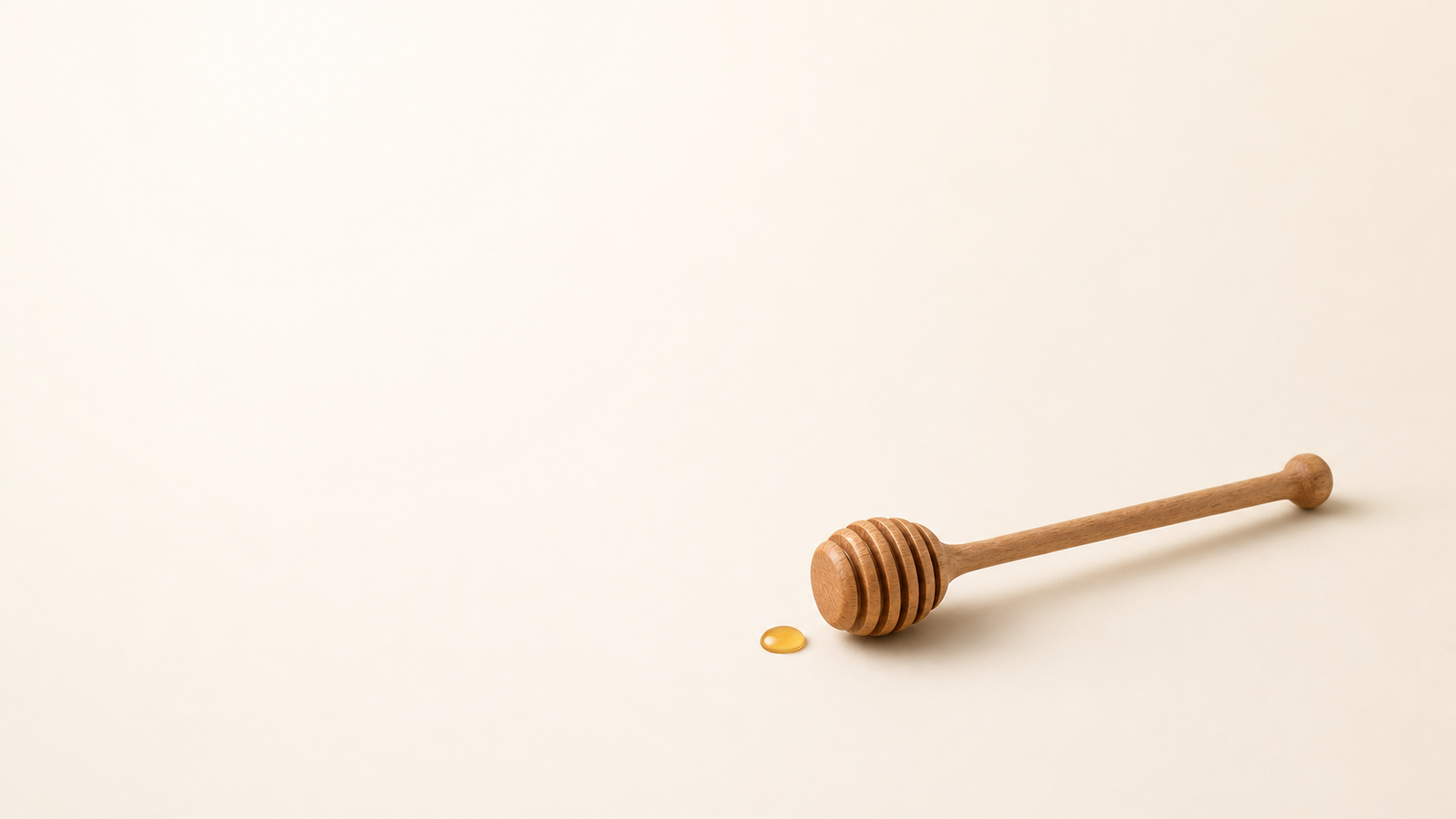 Wooden honey dipper with a drop of golden honey on cream background